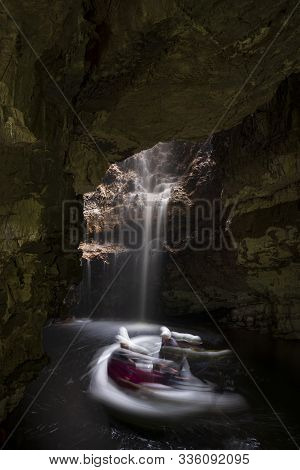 A Slow-shutter-speed Photograph Showing The Movement Of Explorers On A Raft Looking At A Waterfall I