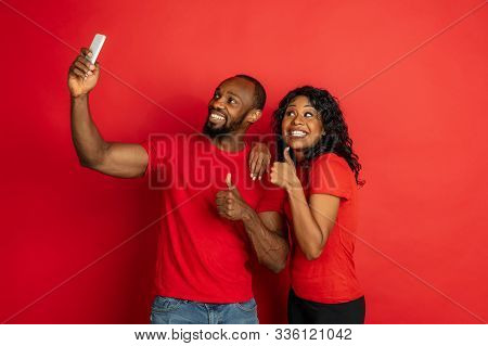 Young Emotional African-american Man And Woman In Bright Casual Clothes Posing On Red Background. Co