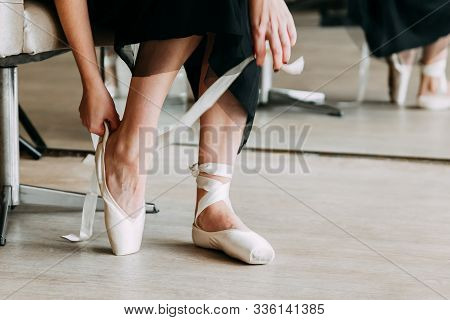 Close-up Shot Of A Ballerina Taking Off The Ballet Shoes Sitting On The Floor In The Studio.