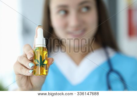 Focus On Female Hand Holding Bottle With Cannabinoid Oil. Beautiful Smiling Lady Wearing Medical Gow