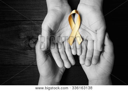 Golden Ribbon Childhood Symbol Of The Fight Against Cancer In Children In Hands On A Dark Background