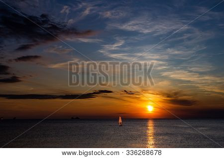 Lonely Wind Surfer Setting Sail Towards The Dramatic And Magnificent Scenic Sunset At The Coast Of T