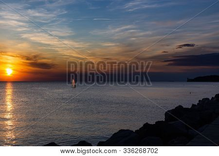 Lonely Wind Surfer Setting Sail Towards The Dramatic And Magnificent Scenic Sunset At The Coast Of T