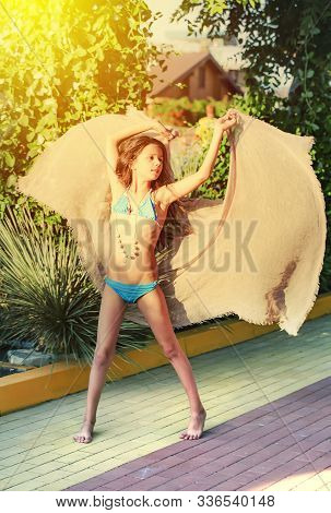 Dancing Young Girl In Blue Swimsuit And With Sandy Beach Poreo Poses On Background Of Greenery And A