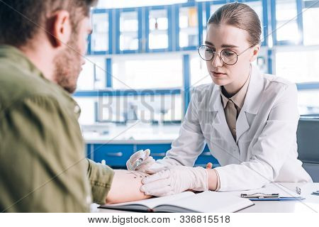 Selective Focus Of Attractive Allergist Holding Syringe Near Man In Clinic