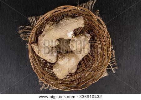 Group Of Two Whole Fresh Brown Ginger In Round Rattan Bowl With Jute Fabric Flatlay On Grey Stone