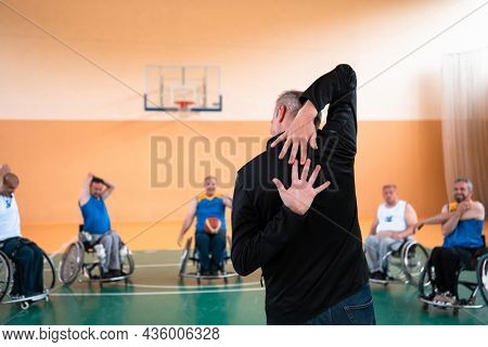the selector of the basketball team with a disability stands in front of the players and shows them the stretching exercises before the start of training