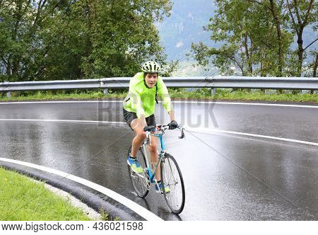 Young Cyclist With Protective Helmet Pedaling Laboriously On The Road With Rain Gear During A Rainy 