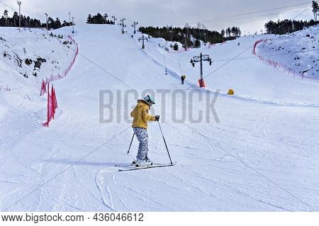 Happy Smiling Young Woman In Yellow Jacket And Ski Helmet Skiing On A Mountain Slope, Winter Sports,