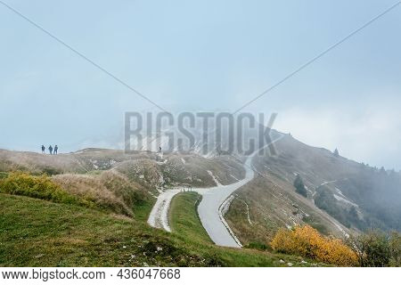 Several People Walk Along The Ridge In Foggy Weather. Misty Mountians Green Landscape With Rural Roa