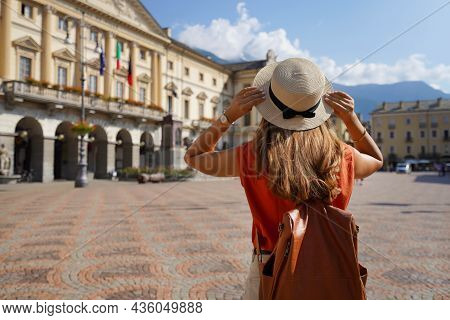 Stylish Traveler Woman Holds Hat On Sunny Day In Aosta City, Italy