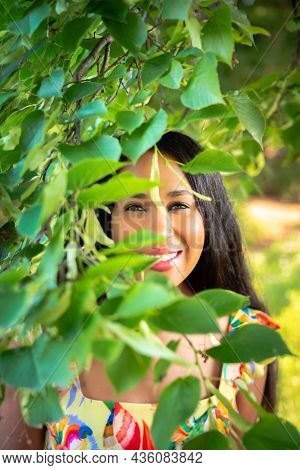 A Beautiful Young Mixed Race African American Woman Smiles With Her Teeth From Behind A Tree Branch 