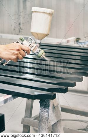 Woman Worker Paints Wooden Furniture Details In Black Color With Spray Gun On Rack Support In Contem