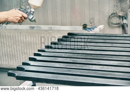 Woman Worker Paints Wooden Furniture Details In Black Color With Spray Gun On Rack Support In Contem