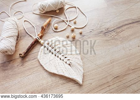 Macrame Leaf  In Natural Color And Thread Windings Lying On A Wooden Table. Cotton Rope Decor Macram