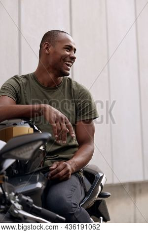 Young black man sitting on sports motorcycle on city street. Concept of trip and journey in personal transport. Guy wearing casual clothes. Vacation, leisure, hobby and enterteiment. Idea of freedom.