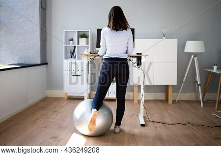 Woman Using Adjustable Height Standing Desk In Office For Good Posture