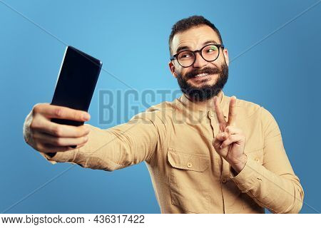 Happy Caucasian Male Wearing Eyeglasses And Beige Shirt, Smiling And Showing V Sign While Taking Sel