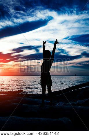 Happy Child Silhouette With Hands Up In The Water On The Sunset Background