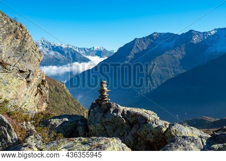 Hiking In Central Switzerland. A Cairn Marking A Footpath, High Mountains In The Background