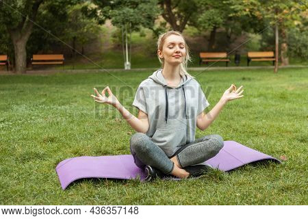 Young Fitness Woman Meditates While Sitting Tna Mat In The Park. Slim Woman Practicing Yoga Pose. He