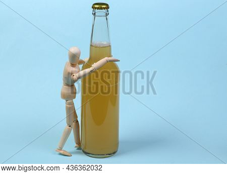 Alcoholism. Wooden Puppet And Bottle Of Beer On Blue Background.