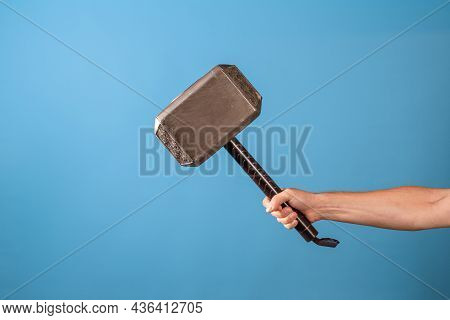 Be A Hero, Perform A Feat. The Scandinavian Hammer Of Thor, Mjolnir In A Mans Hand. Photo On A Blue 