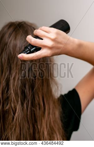 Young Woman Hand Holds Bottle And Spraying Her Wavy Blond Long Hair For Making It Silken And Strong.