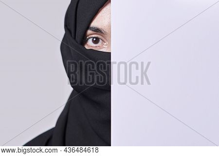 Young Muslim Women With Expressive Eyes Covering Part Of Her Face With White Paper. Muslim Girl In T