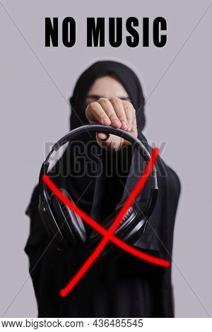 Muslim Woman In Traditional Hijab Clothing Holding Black Wireless Headphones And Crossed Sign With R