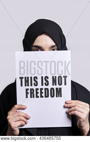Muslim Woman Holding A Paper With Text - This Is Not Freedom. Muslim Woman In Traditional Hijab Clot