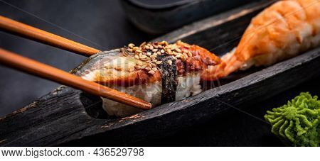 Sushi sashimi set with shrimps and wasabi served with wooden chopsticks on black taable. Traditional japanese meal with rice and seafood closeup