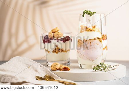 Three Glasses With A Layered Creamy Yoghurt Dessert Trifle With Cookies, Amaretti, Cherries And Thym