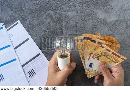 Electricity Costs: Person Checking Electricity Bills With A Light Bulb In One Hand And Several Euro 