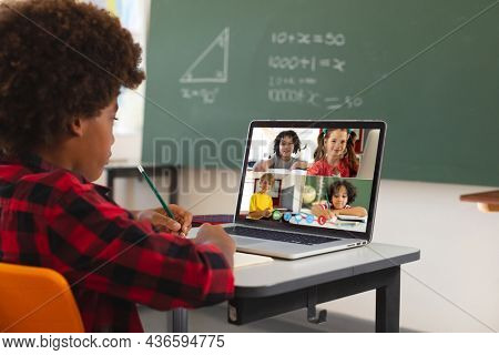African american boy using laptop for video call, with diverse elementary school pupils on screen. communication technology and online education, digital composite image.