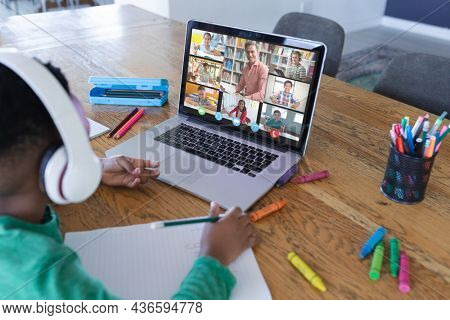 African american boy using laptop for video call, with diverse elementary school pupils on screen. communication technology and online education, digital composite image.