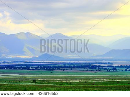 Grassy Steppe Among Blue Mountains In Fog, Cloudy Sunset Sky. Siberia, Russia