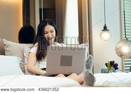 Asian Woman Sitting On Her Bed In Bed With Laptop In Her Bedroom At Home.