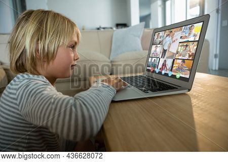 Caucasian boy using laptop for video call, with smiling diverse elementary school pupils on screen. communication technology and online education, digital composite image.
