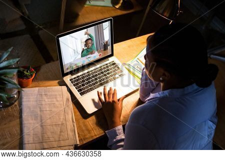 African american woman using laptop for video call, with elementary school pupil on screen. communication technology and online education, digital composite image.