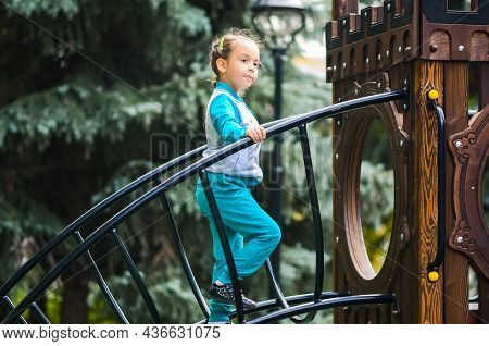 A Little Girl 5 Years Old Plays On The Playground, Passes Through The Staircase Labyrinths In The Da