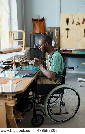Vertical Full Length Portrait Of Young African-american Man In Wheelchair Making Handmade Bag In Lea