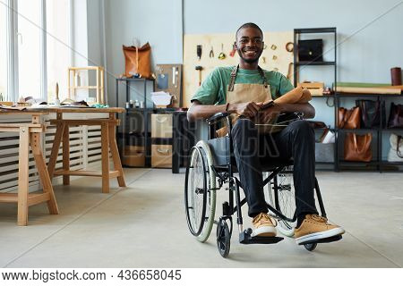 Full Length Portrait Of Smiling African-american Man Using Wheelchair Enjoying Work In Leatherworker