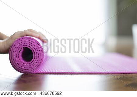 Young Woman Rolling Her Yoga Mat After Exercising And Doing Meditation At Home