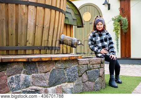 A Girl Sits On A Stone Curb By A Water Tower In A Dwarf Village With Small Colorful Houses, Tervete
