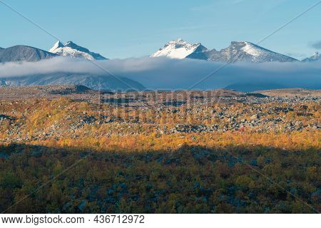 Snow Covered Mountain Peaks Tower Above Thick Layer Of Grey Clouds In Early Morning. Massif Of Ahkka