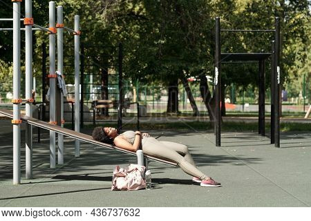 Young restful sportswoman enjoying music in earphones while relaxing on sports facilities on sportsground