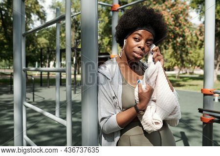 Young sportswoman with soft white towel having rest after training on sportsground