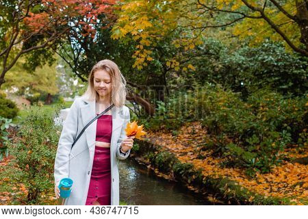 Smiling Romantic Young Woman In Coat Enjoying A Hot Drink In Her Reusable Thermos Cup, Picking Falle