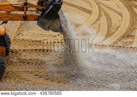 A Bulldozer Pours Gravel From A Bucket Onto The Compacted Sand At A Construction Site - Close-up Vie